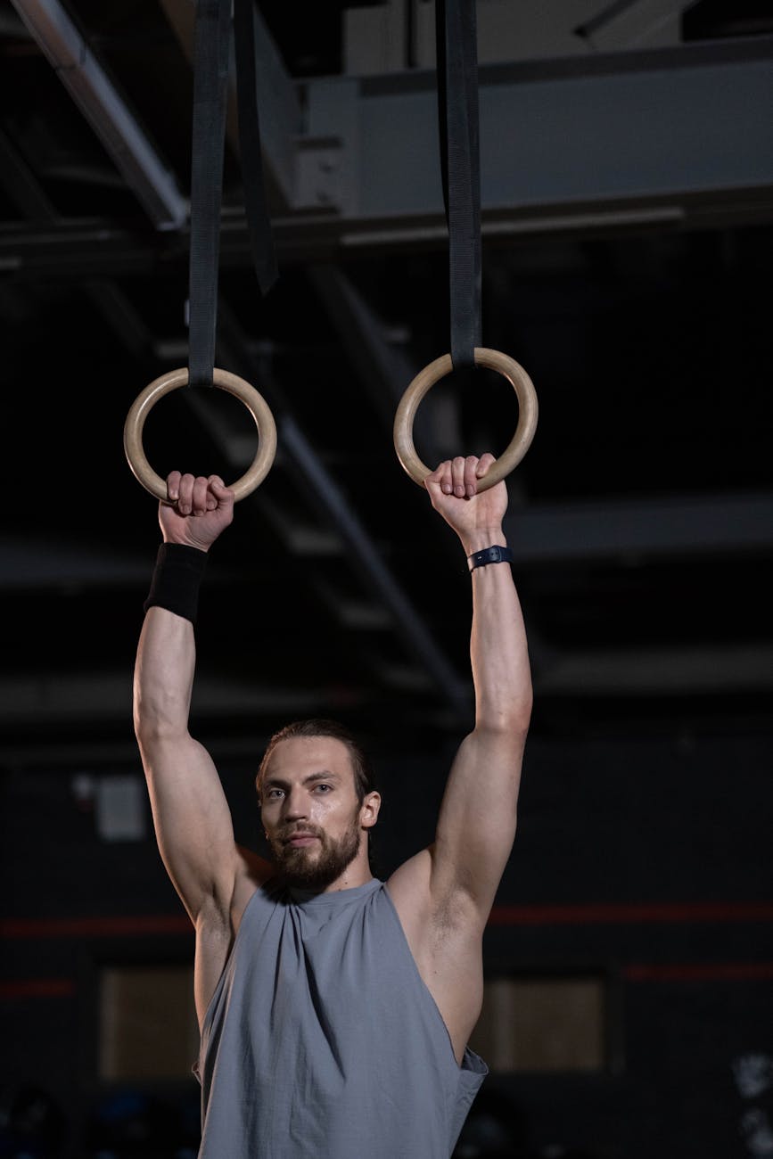 man in gray tank top holding onto gymnastic rings